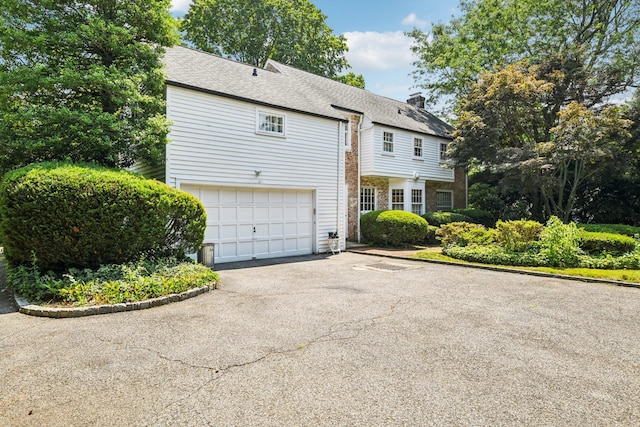 21 Orchard Dr, East Williston, NY 11596 - view of front of house with driveway, an attached garage, a chimney, and a shingled roof