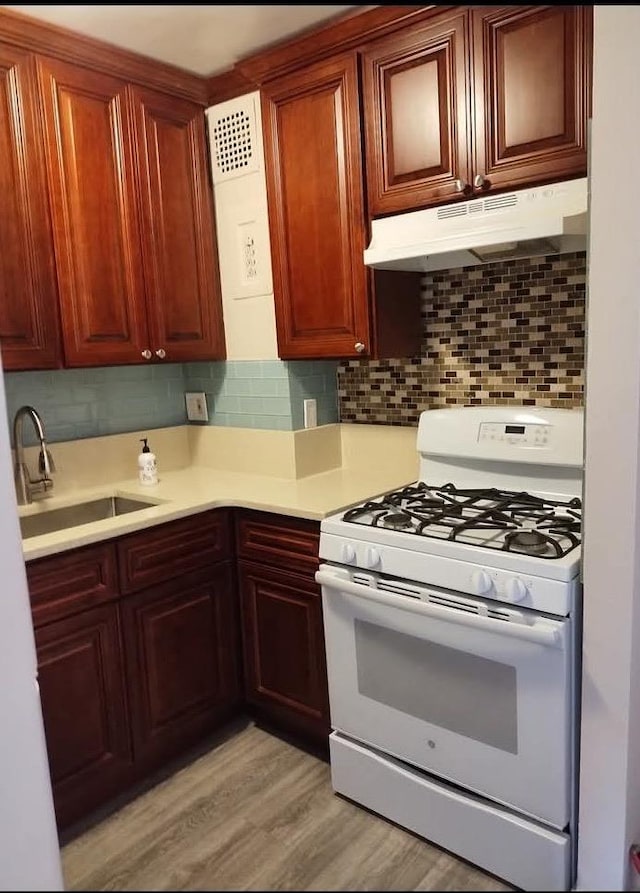 124 Smith St Unit 3B, Freeport, NY 11520 - kitchen with white gas range, under cabinet range hood, light countertops, decorative backsplash, and light wood-style floors