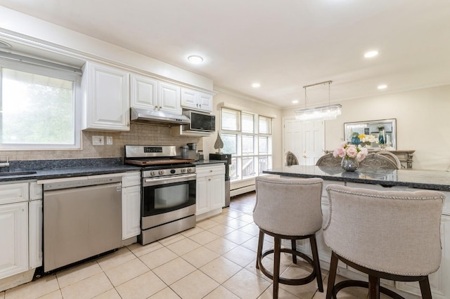 114 Birchwood Park Dr, Syosset, NY 11791 - kitchen with stainless steel appliances, under cabinet range hood, dark countertops, white cabinets, and light tile patterned flooring