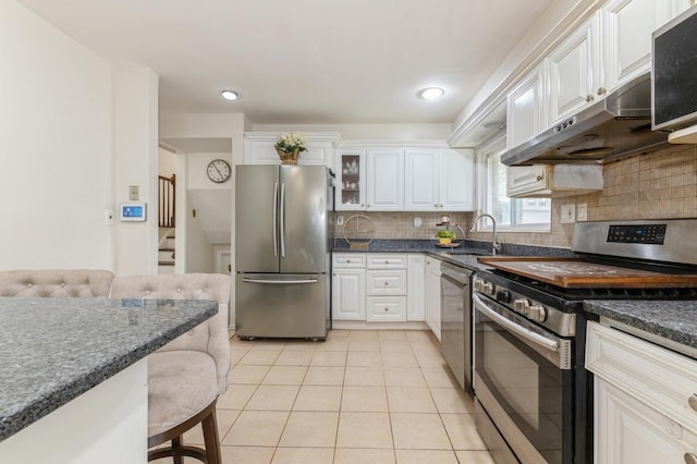 114 Birchwood Park Dr, Syosset, NY 11791 - kitchen featuring stainless steel appliances, light tile patterned flooring, a kitchen bar, white cabinetry, and tasteful backsplash