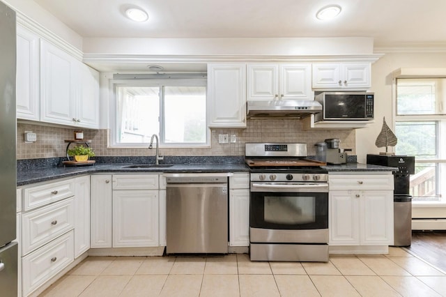 114 Birchwood Park Dr, Syosset, NY 11791 - kitchen with appliances with stainless steel finishes, under cabinet range hood, white cabinetry, light tile patterned floors, and ornamental molding