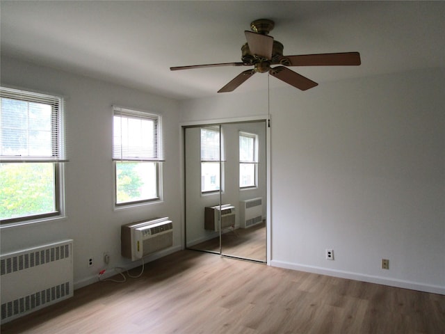 324 Post Ave Apt 8-J, Westbury, NY 11590 - unfurnished bedroom featuring radiator heating unit, a wall mounted AC, light wood-type flooring, a closet, and ceiling fan