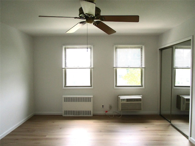 324 Post Ave Apt 8-J, Westbury, NY 11590 - empty room featuring radiator heating unit, a wall mounted AC, wood finished floors, and a ceiling fan
