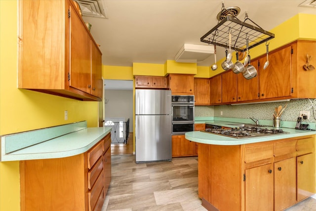 9 Bittersweet Ln, Glen Cove, NY 11542 - kitchen with appliances with stainless steel finishes, light countertops, brown cabinets, a peninsula, and light wood finished floors