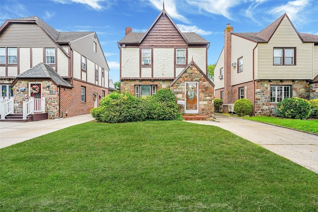 8624 253rd St, Bellerose, NY 11426 - tudor-style house with a front lawn, stone siding, a chimney, and driveway