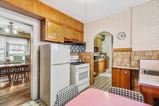 16608 Cryders Ln, Beechhurst, NY 11357 - kitchen with white appliances, under cabinet range hood, wallpapered walls, brown cabinetry, and tile patterned floors