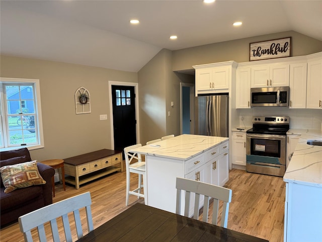 22 Bradish Ln, Babylon, NY 11702 - kitchen featuring appliances with stainless steel finishes, vaulted ceiling, light wood finished floors, a kitchen island, and white cabinetry