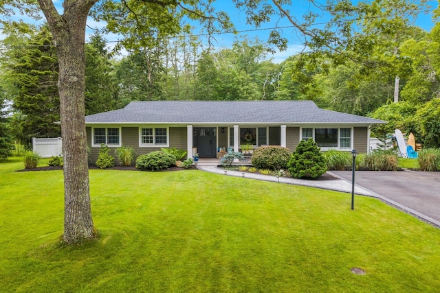 24 Canvasback Ln, East Quogue, NY 11942 - ranch-style house featuring a porch, a front yard, a shingled roof, and driveway