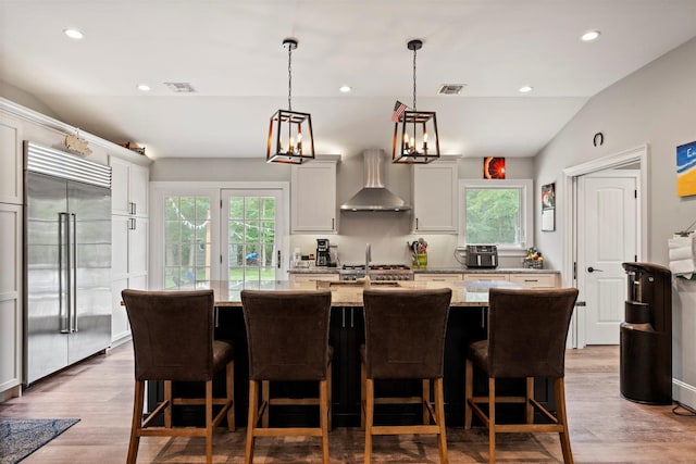 24 Canvasback Ln, East Quogue, NY 11942 - kitchen featuring stainless steel built in refrigerator, healthy amount of natural light, light stone countertops, lofted ceiling, and wall chimney exhaust hood