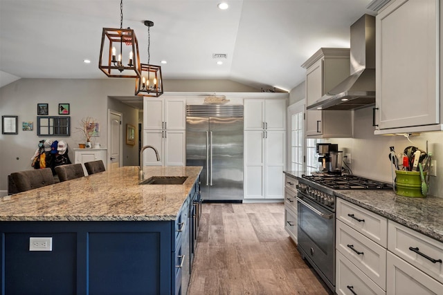 24 Canvasback Ln, East Quogue, NY 11942 - kitchen with lofted ceiling, high quality appliances, wall chimney range hood, blue cabinetry, and light wood-type flooring