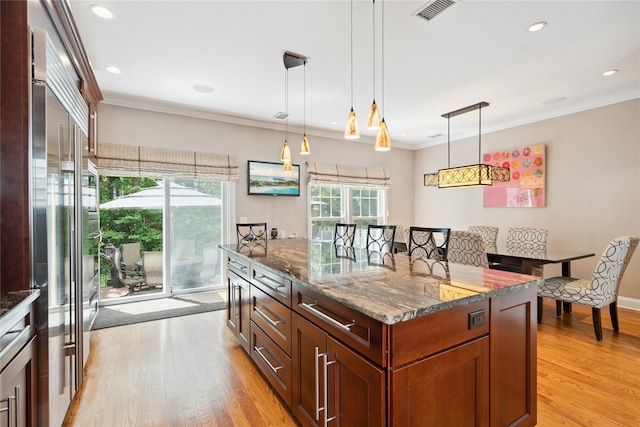 28 The Mews, Syosset, NY 11791 - kitchen featuring ornamental molding, a kitchen island, light wood-type flooring, dark stone counters, and hanging light fixtures