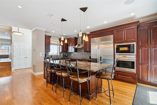 28 The Mews, Syosset, NY 11791 - kitchen featuring built in appliances, wall chimney range hood, ornamental molding, dark brown cabinets, and a breakfast bar area