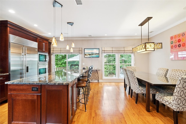 28 The Mews, Syosset, NY 11791 - kitchen featuring built in appliances, a kitchen island, light wood-style floors, dark stone counters, and a breakfast bar area