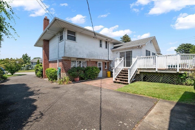 20 Deb St, Plainview, NY 11803 - back of property with a chimney, brick siding, a wooden deck, a lawn, and asphalt driveway