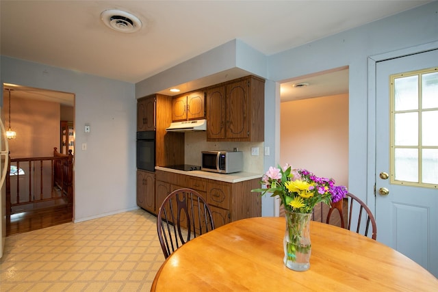 180 Hunter Ave, North Babylon, NY 11703 - kitchen with black appliances, under cabinet range hood, light countertops, light floors, and brown cabinetry