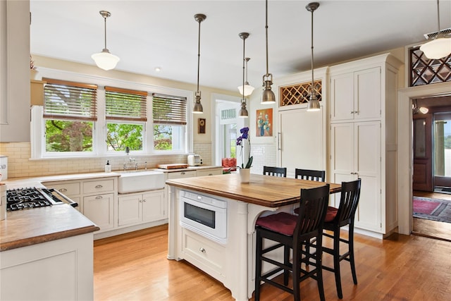 28 Shore Rd, Douglaston, NY 11363 - kitchen featuring backsplash, light wood-type flooring, a breakfast bar, hanging light fixtures, and white cabinetry