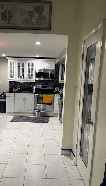 226 14th Ave, West Babylon, NY 11704 - kitchen featuring stainless steel appliances, dark countertops, backsplash, white cabinetry, and light tile patterned floors
