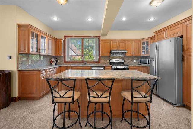 83-14 266th St, Glen Oaks, NY 11004 - kitchen featuring appliances with stainless steel finishes, under cabinet range hood, a kitchen island, a breakfast bar area, and light stone counters