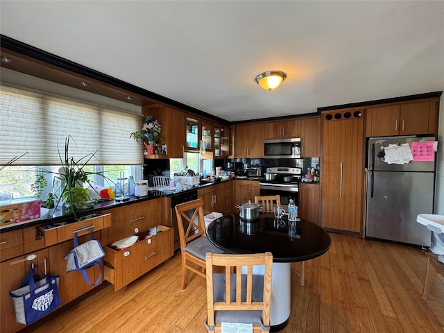 38 Nesaquake Ave, Port Washington, NY 11050 - kitchen featuring appliances with stainless steel finishes, dark countertops, light wood finished floors, and glass insert cabinets