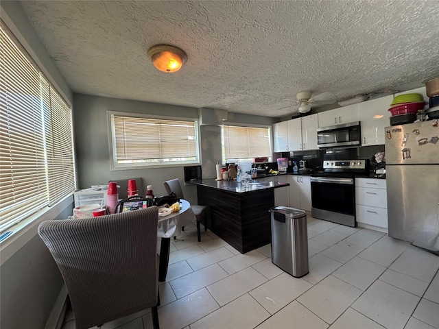 38 Nesaquake Ave, Port Washington, NY 11050 - kitchen with appliances with stainless steel finishes, dark countertops, plenty of natural light, white cabinetry, and a textured ceiling
