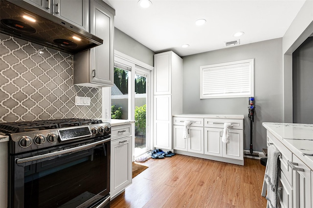 3 Grant Ave, Albertson, NY 11507 - kitchen with gas range, under cabinet range hood, light countertops, decorative backsplash, and light wood finished floors