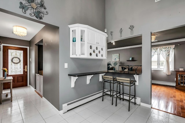 117 E Madison St, East Islip, NY 11730 - kitchen with a baseboard radiator, glass insert cabinets, white cabinetry, a towering ceiling, and light tile patterned flooring