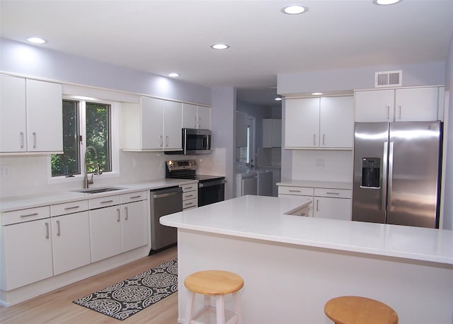 121 Lower Sheep Pasture Rd, East Setauket, NY 11733 - kitchen featuring appliances with stainless steel finishes, a kitchen bar, white cabinets, light wood finished floors, and light countertops