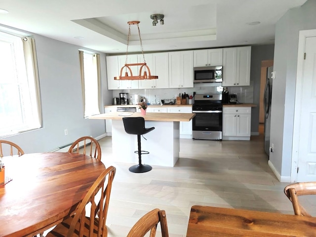 12 Monell Pl, Beacon, NY 12508 - kitchen with stainless steel appliances, white cabinets, a breakfast bar, light wood finished floors, and a tray ceiling