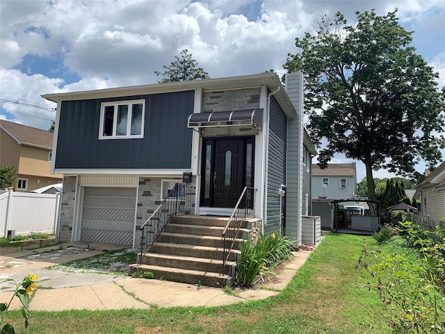 6 2nd Pl, Roosevelt, NY 11575 - view of front of home featuring an attached garage, a chimney, driveway, stone siding, and board and batten siding