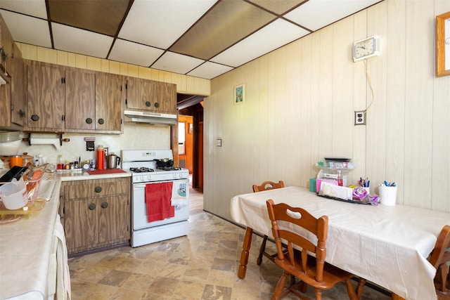 353 W Elm Rd, Mastic Beach, NY 11951 - kitchen featuring gas range gas stove, under cabinet range hood, brown cabinets, wooden walls, and light countertops