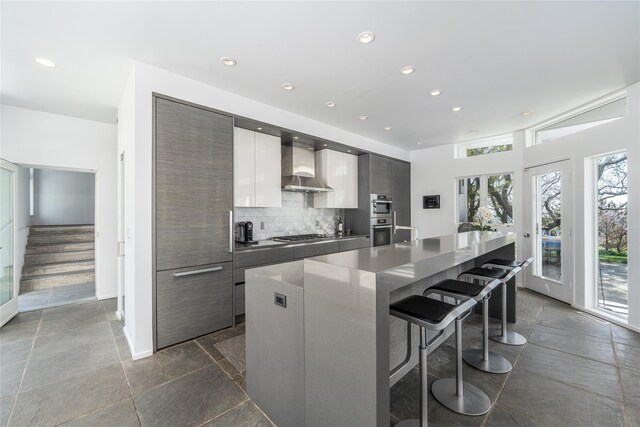 4105 Soundview Ave, Mattituck, NY 11952 - kitchen featuring wall chimney exhaust hood, modern cabinets, a breakfast bar area, backsplash, and recessed lighting