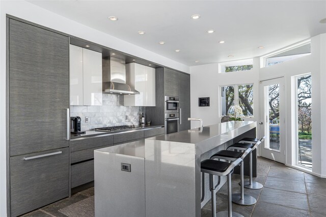 4105 Soundview Ave, Mattituck, NY 11952 - kitchen featuring modern cabinets, wall chimney exhaust hood, a breakfast bar area, recessed lighting, and backsplash