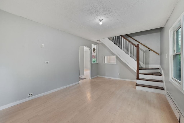 14 Cooper Dr, Nanuet, NY 10954 - unfurnished living room featuring a baseboard heating unit, a textured ceiling, stairway, light wood-style flooring, and plenty of natural light