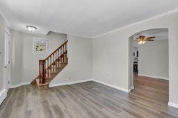 10 Valentine St, Glen Cove, NY 11542 - unfurnished living room with wood finished floors, arched walkways, stairs, ornamental molding, and a ceiling fan