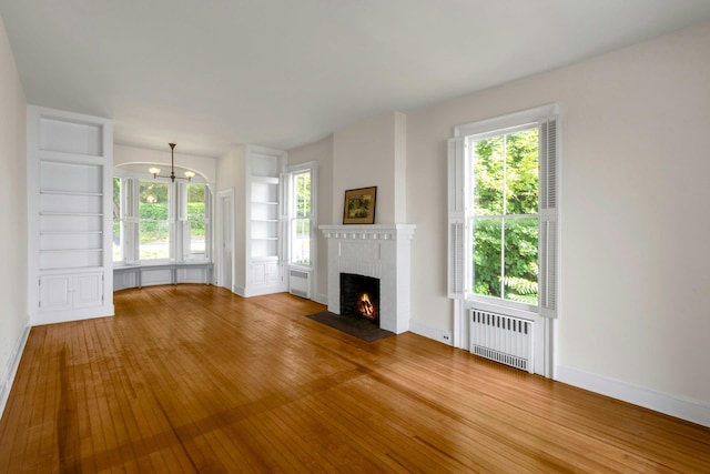 165 River Rd, Nyack, NY 10960 - unfurnished living room featuring radiator, wood-type flooring, a chandelier, built in features, and a brick fireplace
