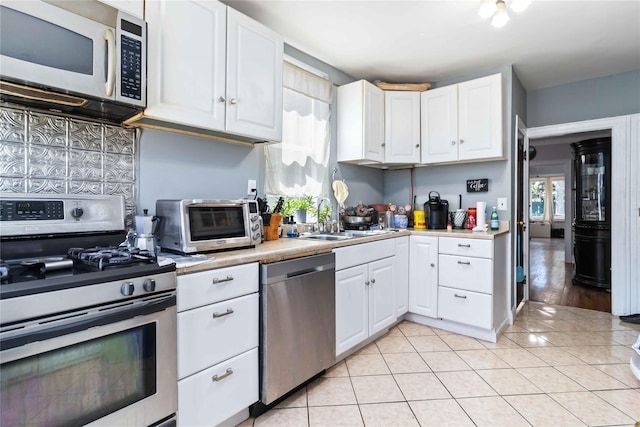 25-57 Mcintosh St, East Elmhurst, NY 11369 - kitchen with appliances with stainless steel finishes, light countertops, white cabinetry, light tile patterned floors, and backsplash