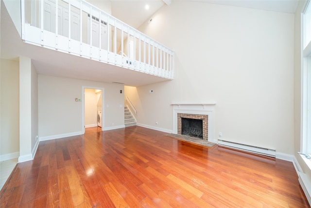 5 Grove Mews, Chappaqua, NY 10514 - unfurnished living room featuring baseboard heating, high vaulted ceiling, wood finished floors, stairway, and a fireplace