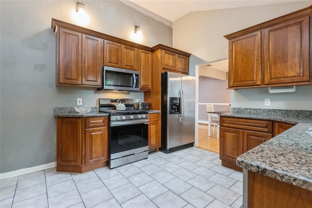 46 Laffin Ln, Poughkeepsie, NY 12603 - kitchen featuring stainless steel appliances, brown cabinetry, vaulted ceiling, dark stone counters, and light tile patterned floors