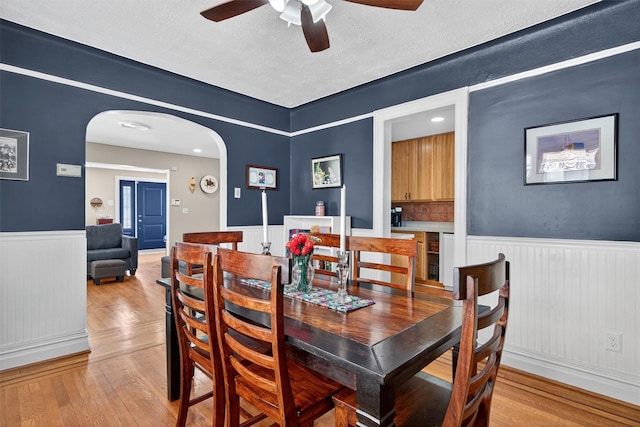 829 Logan Ave, Bronx, NY 10465 - dining area featuring arched walkways, a wainscoted wall, ceiling fan, light wood-style flooring, and a textured ceiling