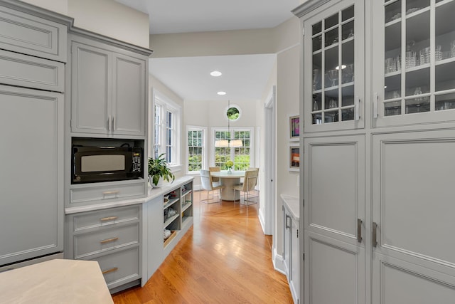77 Haights Cross Rd, Chappaqua, NY 10514 - kitchen with black microwave, gray cabinets, light wood-style flooring, glass insert cabinets, and light countertops