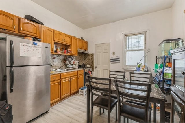 4808 92nd St, Elmhurst, NY 11373 - kitchen with appliances with stainless steel finishes, under cabinet range hood, light wood-type flooring, backsplash, and brown cabinetry