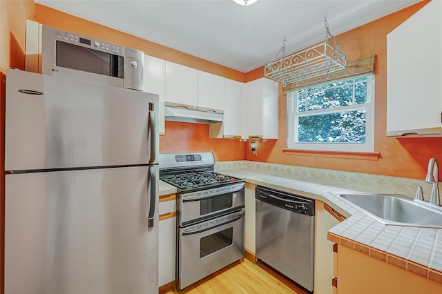 54 Fairharbor Dr Unit 54, Patchogue, NY 11772 - kitchen with stainless steel appliances, white cabinets, range hood, light wood-style floors, and tile countertops