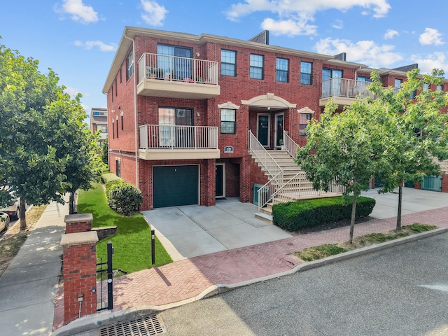 APTA2-22 Constitution Pl Unit 167, College Point, NY 11356 - view of front facade with brick siding, concrete driveway, an attached garage, and a balcony