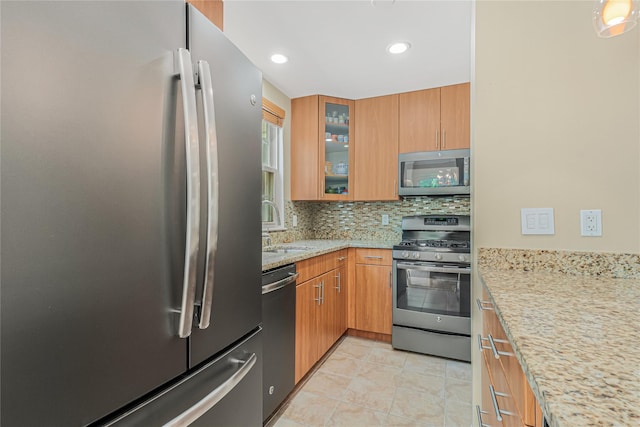 55 Oceana Dr E Unit 1B, Brooklyn, NY 11235 - kitchen with appliances with stainless steel finishes, decorative backsplash, light stone countertops, light tile patterned floors, and glass insert cabinets