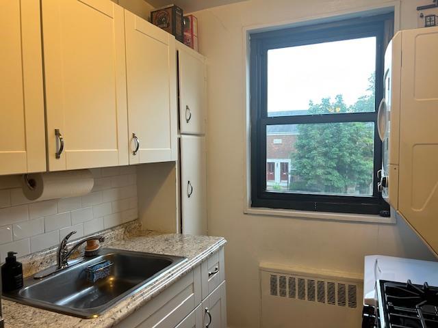 199-39 19th Ave Upper, Upper, Whitestone, NY 11357 - kitchen with stacked washer / dryer, radiator, tasteful backsplash, and plenty of natural light