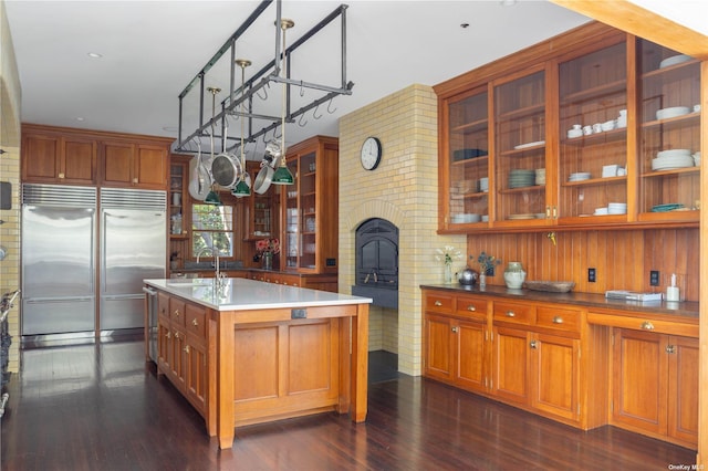 12120 New Suffolk Ave, Cutchogue, NY 11935 - kitchen featuring appliances with stainless steel finishes, dark wood-style flooring, glass insert cabinets, an island with sink, and brown cabinets