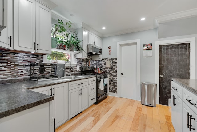 110 Pine Ave, Ossining, NY 10562 - kitchen featuring black range with gas cooktop, stainless steel microwave, dark countertops, decorative backsplash, and light wood-style floors