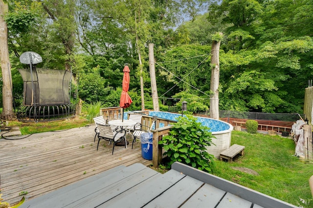 110 Pine Ave, Ossining, NY 10562 - wooden deck featuring an outdoor pool, a trampoline, view of scattered trees, and outdoor dining area