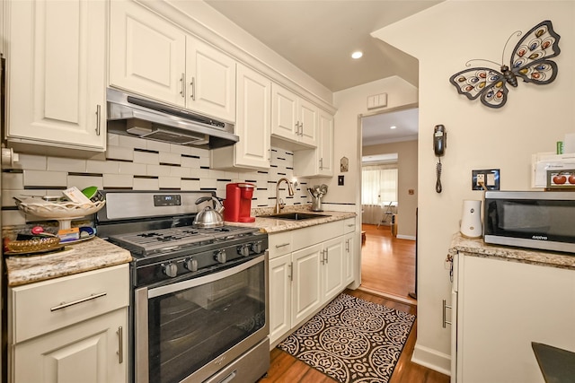 92-05 218th Pl, Queens Village, NY 11428 - kitchen with appliances with stainless steel finishes, under cabinet range hood, wood finished floors, backsplash, and white cabinetry