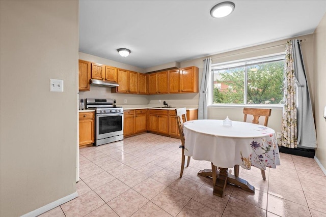 1935 Holland Ave, Bronx, NY 10462 - kitchen featuring gas stove, under cabinet range hood, light countertops, light tile patterned floors, and brown cabinetry